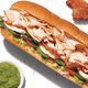 Subway's turkey cali sub with a side of green sauce and three slices of bacon on white background